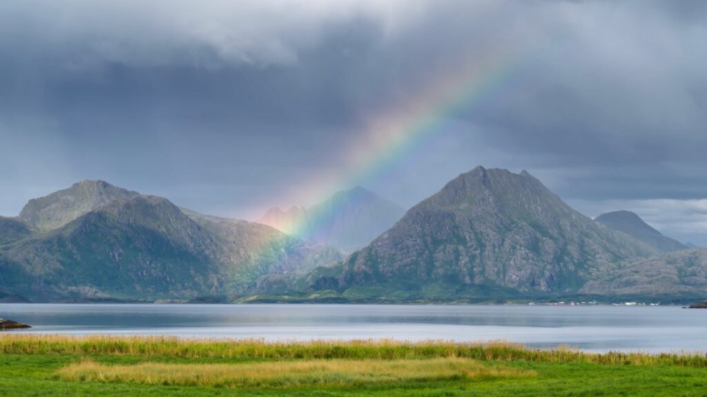 Regenbogen im Fjord vor norwegischen Bergen